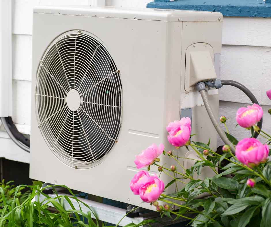 A heat pump outside a home with flowers around it